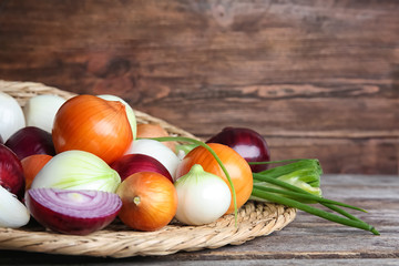 Wicker mat with fresh ripe onions on wooden table