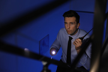 Male security guard with flashlight and portable radio transmitter in dark room