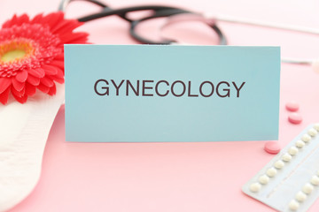 Card with word GYNECOLOGY, menstrual pad and birth control pills on color background