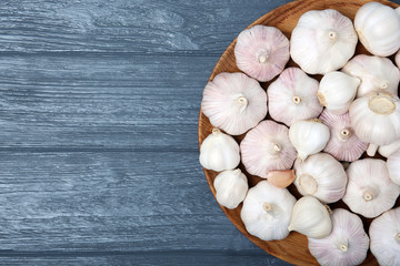 Fototapeta na wymiar Plate with fresh garlic bulbs on wooden background, top view