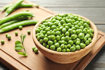 Bowl with green peas on wooden board