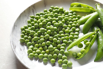 Plate with green peas on light background, closeup