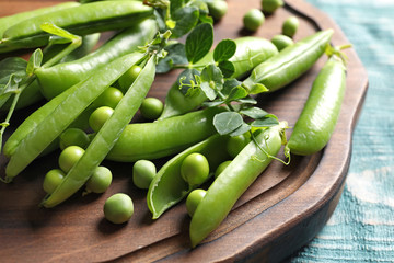 Wooden board with green peas on table, closeup
