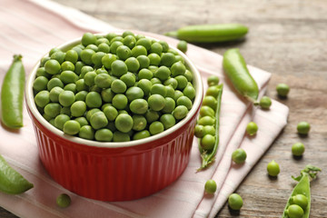 Bowl with green peas on wooden table