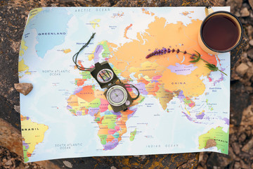 Compass, mug with drink and map on rock outdoors, top view. Camping season
