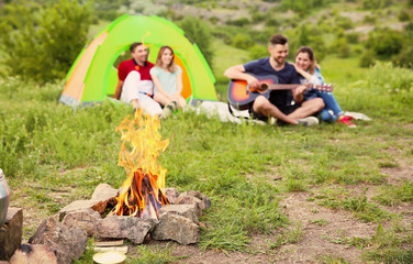 Group of people resting outdoors, focus on bonfire. Camping season