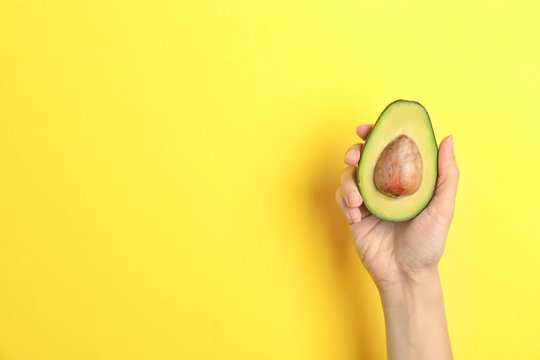 Woman holding ripe cut avocado on color background