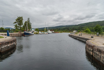 Fort Augustus, Scotland - June 11, 2012: Oich Canal behind the locks. Dock on side has pleasure boats moored, Green hils on horizon under heavy gray sky.