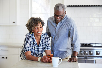 African American Senior Couple looking at cell phone in the kitchen together