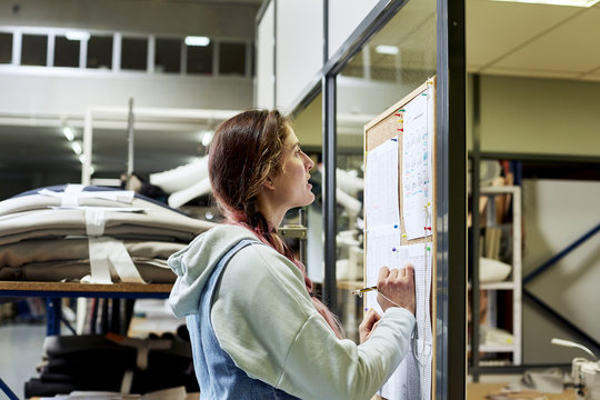 Female Worker Reading Document On Bulletin Board In Sofa Worksho