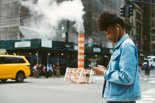 Young Woman With Headphones And Phone In Busy City