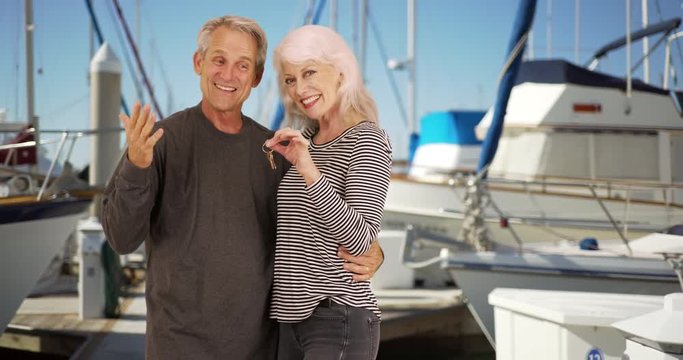 Portrait of happy mature couple holding keys to new sail boat, Retired male and female at the boat dock, smiling at camera, 4k