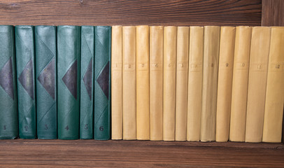 multivolume books of dark green and beige color neatly stacked on a shelf