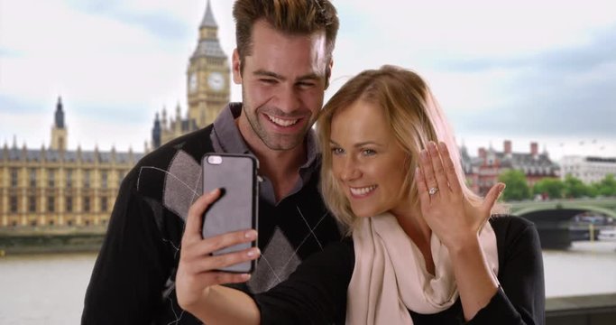 Joyful newly engaged couple take a selfie in London, Man and woman take a picture by the River Thames to share news with friends, 4k