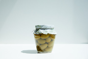 jar of aromatic oil with green olives on white table