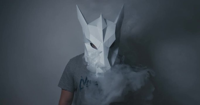 Male wearing dragon head low poly paper craft mask exhaling smoke from a vapor. 4K UHD 60 FPS SLOW MOTION