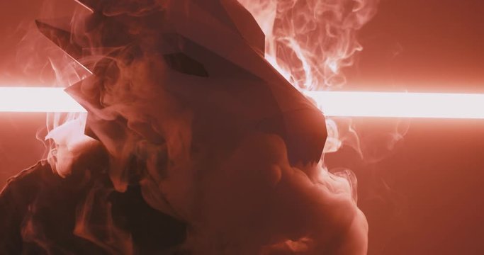 Male wearing dragon head low poly paper craft mask exhaling smoke against bright neon light. 4K UHD 60 FPS SLOW MOTION