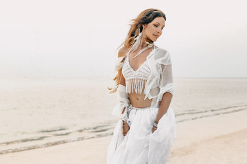 Fototapeta na wymiar beautiful young boho woman in white dress and feathers posing on the beach. bridal concept