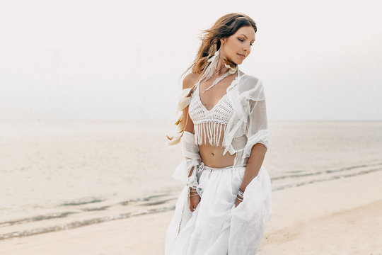 beautiful young boho woman in white dress and feathers posing on the beach. bridal concept