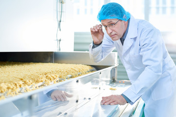 Waist up portrait of senior factory worker checking production process in food industry, standing...