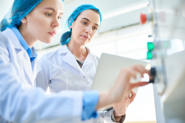 Low angle portrait of  two young female workers wearing lab coats setting up power units and...
