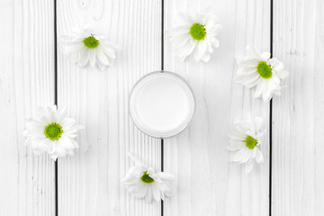 Chamomile cream. Face and body care. Cosmetics in small jar near chamomile flowers on white wooden background top view pattern