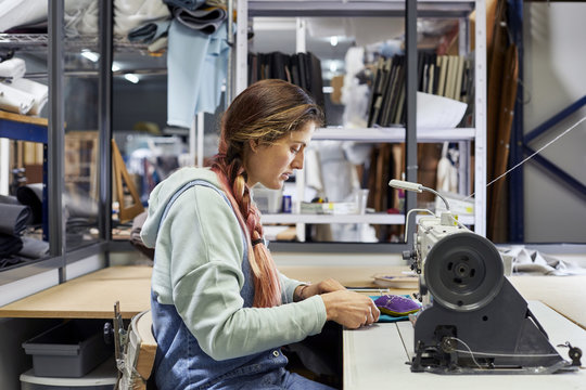 Female Worker Stitching Fabric At Workbench In Sofa Workshop