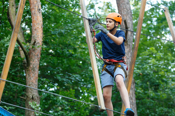 Naklejka na ściany i meble yound kid, sporty boy in helmet with climbing equipment in the rope amusement park. Summer camp, holidays 