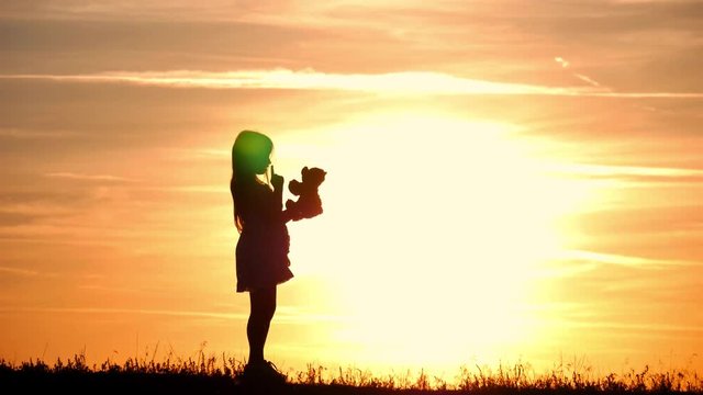Little girl with teddy bear at sunset. Silhouette girl holding a bear doll bear watching the sunset. Concept big dream.