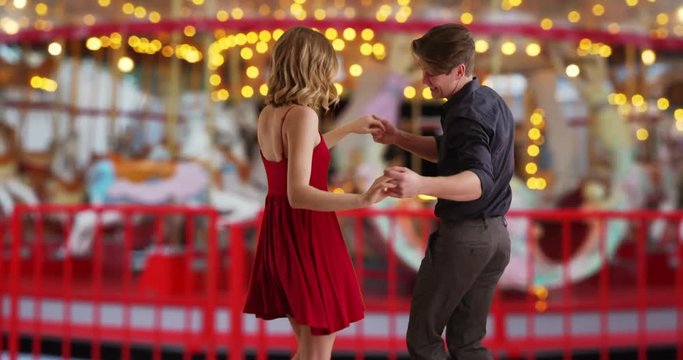 Happy carefree young couple dancing by a merry-go-round, Caucasian man and woman enjoy fun date smiling, 4k