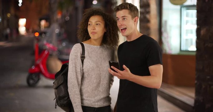 Caucasian male and African female use smartphone for directions in Florence, Portrait of millennial tourists using map on cellphone at night, 4k