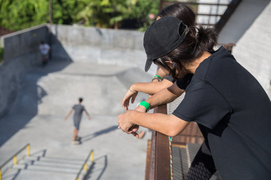 Two teenagers watch their friends skateboarding at a local skate park