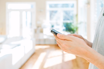 Man's hands using a smartphone on a bright interior background