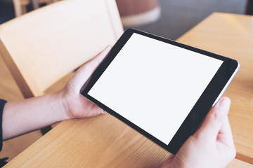 Mockup image of hands holding black tablet pc with blank white desktop screen on wooden table