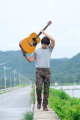 Guy with guitar standing on the dam,  cargo pants