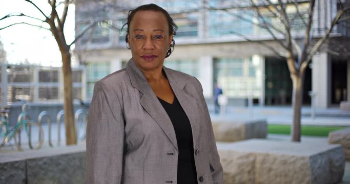 Mature businesswoman poses for portrait outside, Happy African American woman in business suit smiles at camera, 4k