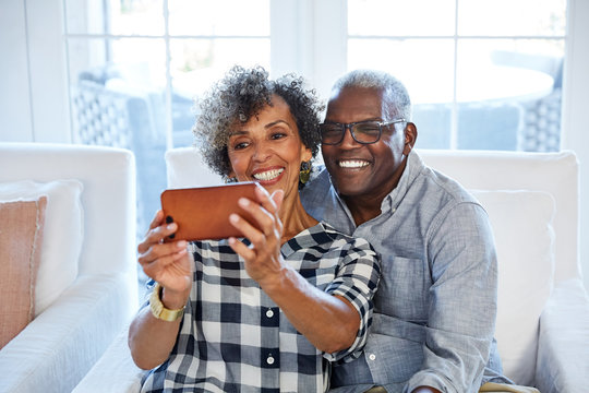 African American senior couple taking a selfie with a camera phone in their living room at home