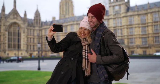 Loving young couple take a selfie in front of Westminster Palace, Portrait of male and female tourists taking a picture on vacation in London, 4k
