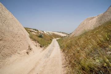 Walking unpaved rough sand trail route through desert mountain grass  landscape of dried ancient red valley with clear sky background, Cappadocia