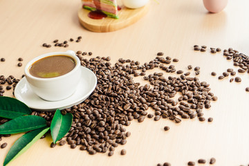 Cup of coffee on coffee beans and leaf on the wooden table with copy space. 