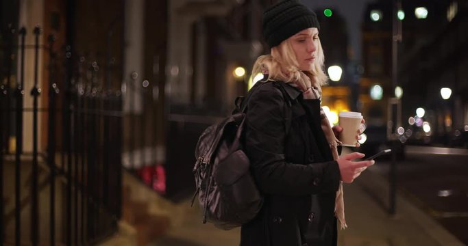 Modern young lady using phone app to get directions after getting lost in city, White woman figuring out directions with smartphone on city sidewalk at night, 4k