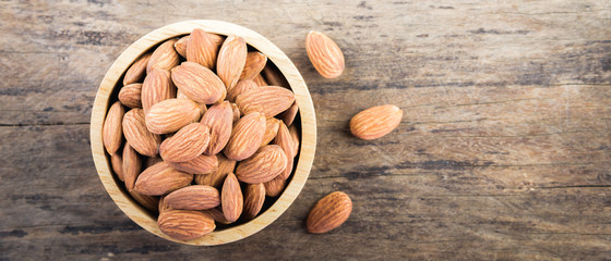 Almonds in brown bowl on textured wooden background.