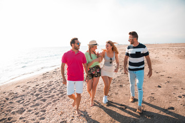 Group of happy young people walking at the beach on beautiful summer sunset. Friends and holiday concept