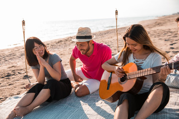 Happy multiracial young people playing guitar and making picnic at the beach. Friends, music and holiday concept.