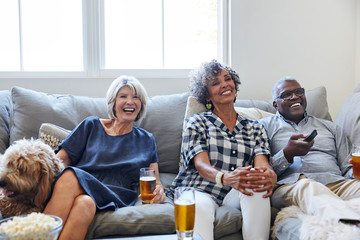Multiethnic seniors drinking, socializing and watching TV together at home