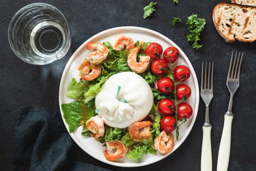 Salad with burrata cheese, shrimps, lettuce and tomatoes. Table top view. Salad on dark background. Healthy italian salad