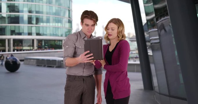 Two young businesspeople using a digital tablet, Caucasian male and female office worker using touchpad outside building, 4k