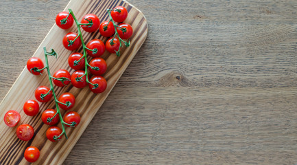 A branch of cherry tomatoes on wooden cutting board. selective focus . pattern with place for text. top view