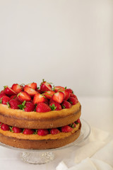 Homemade strawberry cake on a glass stand on the white background.