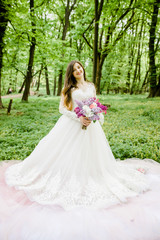Fototapeta na wymiar A sweet bride in a white dress is in the park with a bouquet in her hands